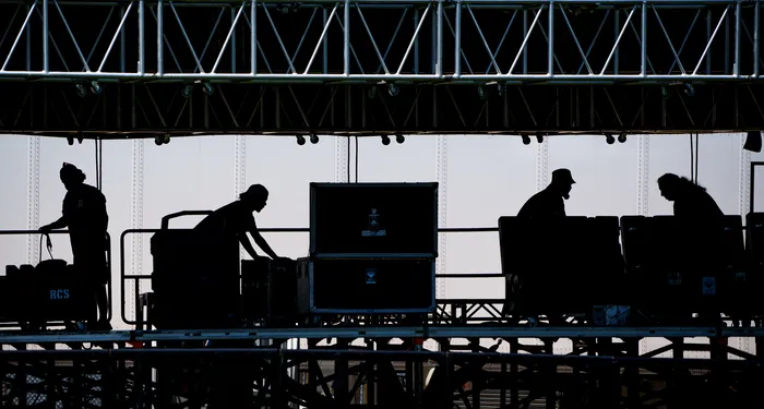Crew silhouettes building a stage under a lighting truss